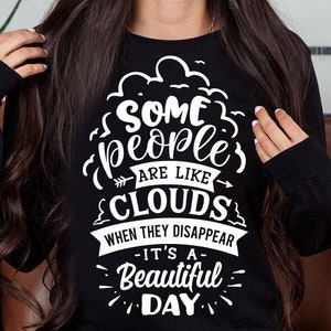 Op de afbeelding: Een zwart shirt met lange mouwen met een wit grafisch ontwerp met de tekst "Sommige mensen zijn als wolken. Als ze verdwijnen, is het een prachtige dag."