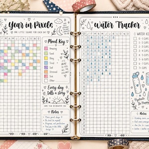May include: A planner open to two pages featuring a Year in Pixels mood tracker and a Water Tracker. The pages include hand-drawn illustrations, grids for daily logging, color-coded mood keys, and notes sections with text like Hydrate Be Happy.