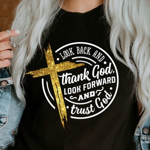 Może przedstawiać: Czarna koszulka z błyszczącym złotym krzyżem i napisem "Look Back and Thank God, Look Forward and Trust God" w białym okrągłym wzorze. Koszulka zawiera r&oacute;wnież ikony typ&oacute;w plik&oacute;w.