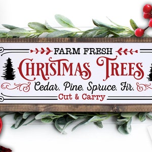 Może przedstawiać: Biały znak z czarnymi i czerwonymi literami, na którym widnieje napis "FARM FRESH CHRISTMAS TREES Cedar. Pine. Spruce. Fir. Cut & Carry." Znak jest oprawiony w drewno i ma rustykalny wygląd.
