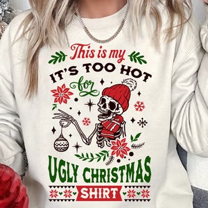 May include: White sweatshirt with a Christmas-themed design featuring a skeleton wearing a Santa hat and holding a Christmas ornament. The text on the sweatshirt reads "This is my It's too hot for Ugly Christmas Shirt".