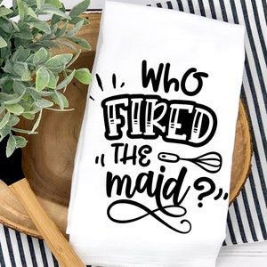 May include: White kitchen towel with black text that reads "Who fired the maid?" with a whisk and spoon graphic.