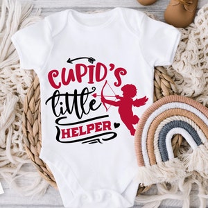 May include: White baby onesie with the text "Cupid's little helper" in black and red lettering. A red silhouette of Cupid with an arrow is next to the text.