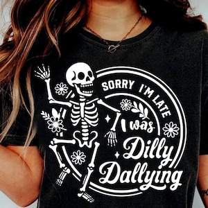以下が含まれることがあります： 白いスケルトンと花柄のデザインが施された黒いTシャツで、「Sorry I'm Late, I was Dilly Dallying」の文字が入っています。「SVG、DXF、PNG、EPS」とブランド名「Black Cats」も含まれています。
