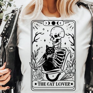Puede incluir: Ilustraci&oacute;n en blanco y negro de un esqueleto sosteniendo un gato negro. La imagen est&aacute; en el estilo de una carta de tarot e incluye el texto "The Cat Lover".