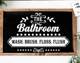 May include: A framed black sign with white text that reads "THE Bathroom WASH. BRUSH. FLOSS. FLUSH." The sign has a dark brown wooden frame and decorative elements. The upper right corner has a white square with text.