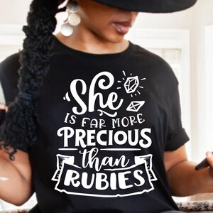 May include: Black t-shirt with white text that reads "She is far more precious than rubies" with a diamond graphic above the text.