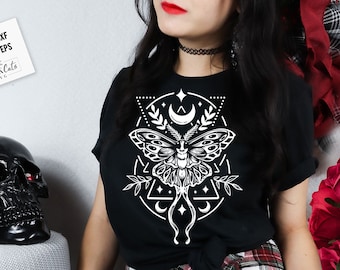 May include: A black t-shirt with a white graphic design of a moth with geometric shapes and crescent moons. The design is centered on the shirt.