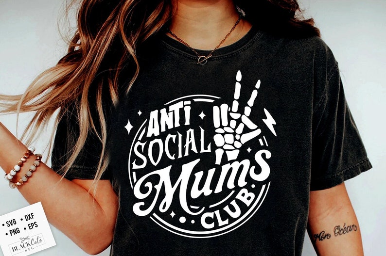 Op de afbeelding: Zwart T-shirt met een witte cirkelvormige afbeelding met de tekst "Anti Social Mums Club" en een skelet hand die een peace-teken maakt.