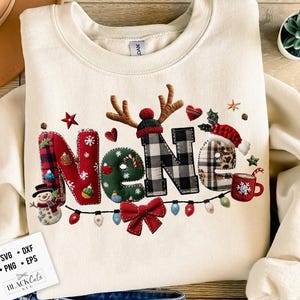 以下が含まれることがあります： クリーム色のスウェットシャツ。クリスマスデザインで「Nene」の文字が描かれています。文字はチェック柄、緑、雪だるまで装飾されています。電飾と赤いリボンがホリデーテーマを完成させています。