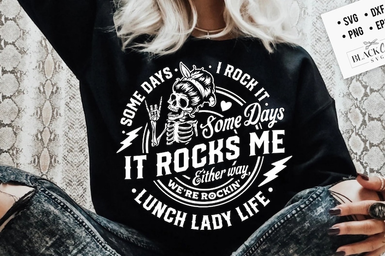 Może przedstawiać: Czarny t-shirt z czarno-białym wzorem graficznym przedstawiającym szkielet z kokiem na głowie, kt&oacute;ry pokazuje znak rock and rolla. Tekst brzmi "Some days I rock it. Some days it rocks me. Either way, we're rockin'. Lunch Lady Life."