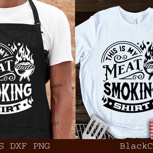 May include: Black apron and white t-shirt with the text "THIS IS MY MEAT SMOKING SHIRT" in a circular design with a grill graphic. The apron is worn by a person. The t-shirt is on a wooden surface.