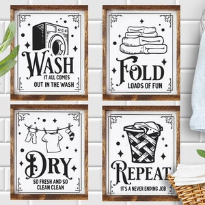 Op de afbeelding: Vier zwart-witte borden met een rustieke houten lijst. De borden hebben illustraties en tekst met een was-thema. De borden lezen "Wash It All Comes Out In The Wash", "Fold Loads Of Fun", "Dry So Fresh And So Clean Clean", en "Repeat It's A Never Ending Job".