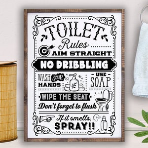 May include: Black and white sign with the text "Toilet Rules" and instructions for bathroom etiquette, including "Aim Straight", "No Dribbling", "Wash Your Hands", "Use Soap", "Wipe the Seat", "Don't forget to flush", and "If it smells, Spray!!".