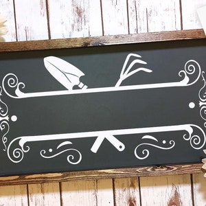 Puede incluir: Un letrero en blanco y negro con temática de jardinería. El letrero tiene una pala y un rastrillo cruzados. El letrero tiene un espacio en blanco para texto y está enmarcado en un marco de madera oscura.