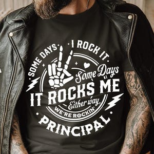 Może przedstawiać: Czarny t-shirt z białym napisem "Some Days It Rocks Me, Some Days I Rock It, Either Way We're Rockin' Principal". Koszulka jest noszona pod czarną skórzaną kurtką. Biały kwadrat z tekstem "SVG, DXF, PNG, EPS" znajduje się na zdjęciu.