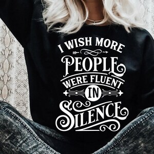 Könnte beinhalten: Ein schwarzes Sweatshirt mit weißem Text, der "Ich wünschte, mehr Menschen wären im Schweigen geübt" lautet.
