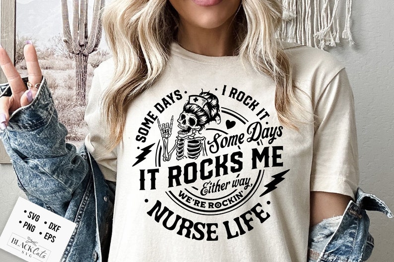 Peut inclure: Un t-shirt blanc avec un motif graphique noir repr&eacute;sentant un squelette portant une coiffe d'infirmi&egrave;re et faisant un geste de rock and roll. Le texte dit "Some days I rock it, Some days it rocks me, Either way, we're rockin', Nurse Life."