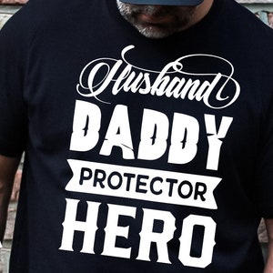 Puede incluir: Camiseta negra con texto blanco que dice "Husband Daddy Protector Hero".