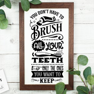 May include: A white sign with a brown wooden frame, featuring a black and white graphic with the text "You don't have to brush all your teeth, only the ones you want to keep."
