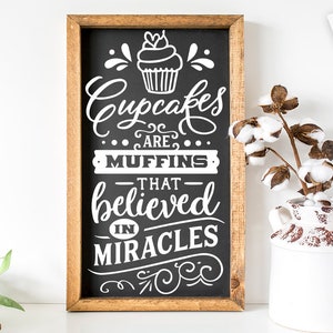 Pode incluir: Uma placa de madeira com fundo de quadro negro. A placa tem texto branco que diz "Cupcakes are muffins that believed in miracles". Há um gráfico de cupcake na parte superior da placa.