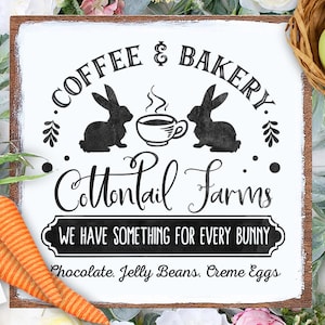 Pode incluir: Uma placa de madeira branca com texto preto que diz "Coffee & Bakery Cottontail Farms We Have Something For Every Bunny Chocolate. Jelly Beans. Creme Eggs". A placa apresenta duas silhuetas de coelhos pretos e uma xícara de café fumegante.