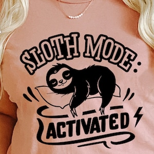 May include: A pink t-shirt with a black graphic design that says "Sloth Mode: Activated" with a cartoon sloth sleeping on a pillow.
