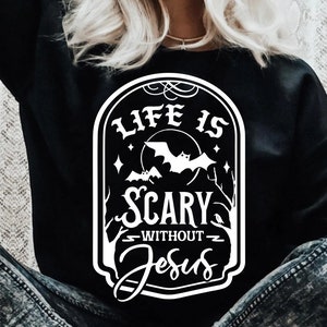 May include: A black t-shirt with a white graphic design that says "Life is Scary Without Jesus". The graphic is in the shape of a vintage sign with bats and a moon.