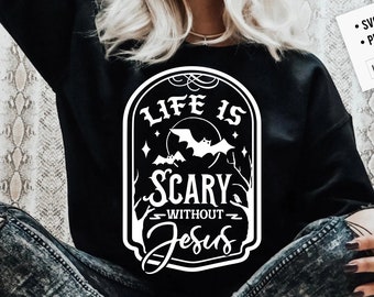 May include: A black t-shirt featuring a white graphic design that reads "Life is Scary Without Jesus". The graphic is in the style of a vintage sign with bats and a moon.