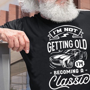 May include: Black t-shirt with white text that reads "I'm not getting old, I'm becoming a classic."  The text is surrounded by a graphic of a classic car.