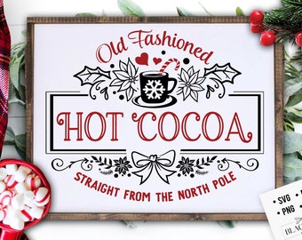May include: A white sign with black and red text that reads "Old Fashioned HOT COCOA STRAIGHT FROM THE NORTH POLE". The sign is framed in wood and has a black and white illustration of a mug of hot cocoa with a candy cane and snowflakes.