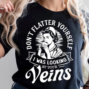 Puede incluir: Camiseta negra con texto blanco que dice "No te hagas ilusiones, estaba mirando tus venas". El texto está rodeado de un círculo con una imagen de dibujos animados de una enfermera sosteniendo una taza.