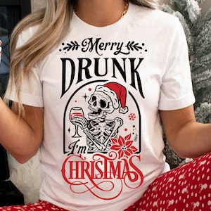 Könnte beinhalten: Weißes T-Shirt mit einem schwarzen und roten Grafikdesign. Die Grafik zeigt ein Skelett, das einen Weihnachtsmann-Hut trägt und ein Glas Wein hält. Der Text "Merry Drunk I'm Christmas" ist in einer festlichen Schrift geschrieben.