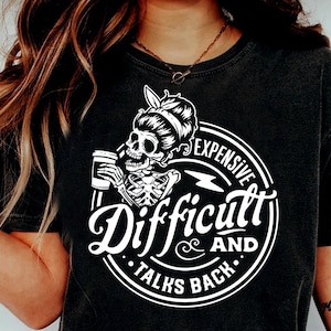 May include: Black and white graphic design of a skeleton with a bun holding a coffee cup. The design is in a circle with the text "Expensive and Difficult Talks Back".