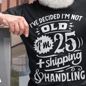 May include: Black t-shirt with the text "I'VE DECIDED I'M NOT OLD I'M 25 + shipping & HANDLING" in white. The shirt is worn by a person with tattoos on their arm.