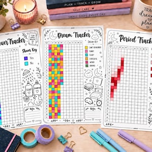 May include: Three printed paper trackers titled Shower Tracker, Dream Tracker, and Period Tracker. Each sheet features a grid for months and days, color-coded keys, and black and white line art illustrations of daily items like soap, pillows, and mugs.