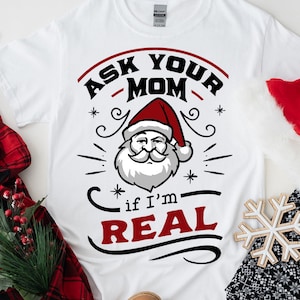 May include: White t-shirt with a red and black graphic design that says "Ask Your Mom if I'm Real" with a cartoon image of Santa Claus.