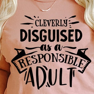 Pode incluir: Uma camiseta rosa com texto preto que diz "Cleverly Disguised as a Responsible Adult".