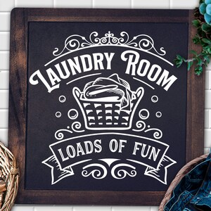 May include: A black chalkboard sign with white text that reads "Laundry Room Loads of Fun". The sign features a vintage-style illustration of a laundry basket with clothes inside.