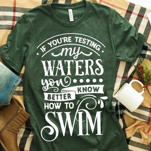 May include: Green t-shirt with white text that reads "If you're testing my waters you better know how to swim".