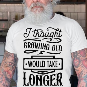 Puede incluir: Una camiseta blanca con texto negro que dice "Pensé que envejecer llevaría más tiempo".