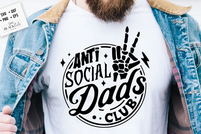 May include: A white t-shirt with a black graphic design that says "Anti Social Dad's Club" in a vintage style font. The graphic also includes a skeleton hand making a peace sign.