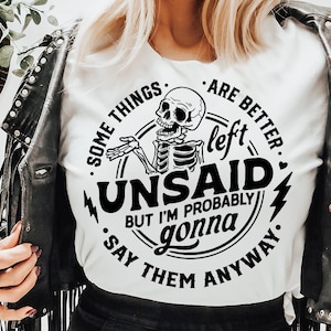 May include: A white t-shirt with a black and white graphic design featuring a skeleton with the text "Some things are better left unsaid, but I'm probably gonna say them anyway."