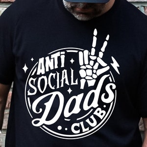 May include: A black t-shirt with a white circle graphic that says "Anti Social Dad's Club". A skeleton hand with a peace sign is in the center of the circle.