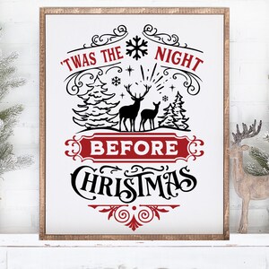 May include: A white sign with a red banner that reads 'Twas the Night Before Christmas'. The sign features a black silhouette of two deer in a snowy forest with pine trees. The sign has a decorative border with swirls and a snowflake.