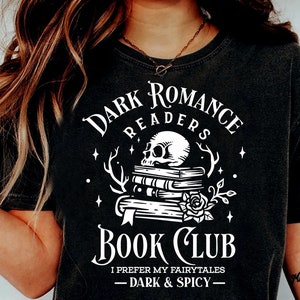 Peut inclure: Un t-shirt noir avec un motif blanc qui dit "Dark Romance Readers Book Club" avec un crâne et une pile de livres. Le texte sous le graphique dit "I prefer my fairytales - dark & spicy -"