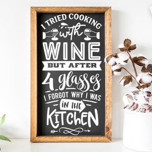 May include: A black chalkboard sign with white text that reads "I tried cooking with wine but after 4 glasses I forgot why I was in the kitchen". The sign is framed in wood and is hanging on a white wall.