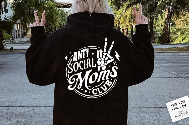 Op de afbeelding: Zwarte hoodie met een wit grafisch ontwerp met de tekst "Anti Social Moms Club" met een skelet hand die een peace-teken maakt.