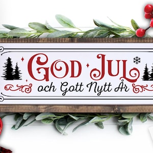 May include: A white wooden sign with a red and black design. The sign says "God Jul och Gott Nytt Ar" which translates to "Merry Christmas and Happy New Year".