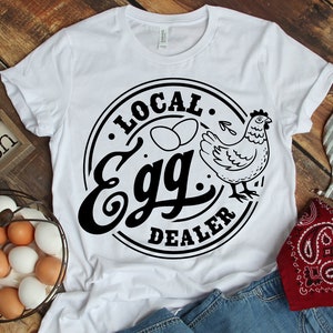May include: White t-shirt with a black circle design that says "Local Egg Dealer" with a chicken and two eggs inside the circle.